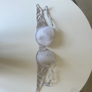 Vit spets-bh med vadderade kupor - Säljer en vit bh med vadderade kupor och fina spetsdetaljer. Axelbanden är justerbara och materialet är mjukt och bekvämt. Perfekt för dig som vill ha en feminin och stilren look.