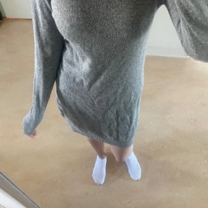 Grå stickad långärmad klänning - Mysig grå stickad klänning med lång ärm och ribbade muddar vid ärmslut och nederkant. Klänningen har en rak passform och är perfekt för kyligare dagar. Enkel och stilren design som passar till många tillfällen.