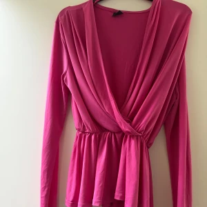Rosa omlottopp från Gina Tricot - Säljer en snygg rosa omlottopp från Gina Tricot med långa ärmar och markerad midja. Toppen har ett djupt omlottliv och är tillverkad i ett mjukt, stretchigt material.   Supersnygg och passar perfekt både till festliga tillfälllen och till sena sommarkvällar! Använd enstaka gånger och är i superfint skick.