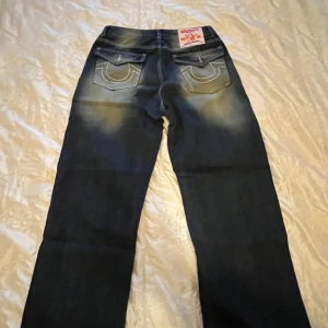 Mörkblå jeansbyxor från True Religion - Säljer min syrras  mörkblå jeansbyxor från True Religion med tydliga kontrastsömmar och stora bakfickor med broderad logga. Byxorna har en klassisk femficksdesign,dessutom är den mer som  bootcut/baggy.inte säker om de är äkta ‼️pris går att diskuteras