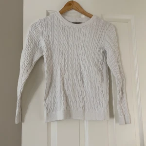 Vit kabelstickad tröja från Basic You - Säljer en vit kabelstickad tröja från Basic You i ekologisk bomull. Tröjan har rund halsringning och långa ärmar, perfekt för lager-på-lager. Klassisk och enkel design som passar till mycket.