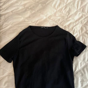 Svart ribbad topp och byxa från Nelly  - Säljer en svart ribbad topp från NLY One i storlek XS. T-shirten har rund halsringning och korta ärmar. Perfekt för dig som gillar en enkel men stilren look. Byxorna är i mjukt material, matchande med toppen. Byxorna är i lång och rak modell.