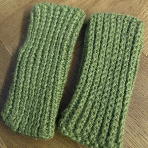Gröna stickade fingerlösa handvärmare - Stickade fingerlösa armvärmare i en mjuk grön nyans. Vantarna har ribbstickat mönster och ett hål för tummen, vilket gör dem smidiga och bekväma att bära. Perfekta för kyliga dagar när du vill ha fingrarna fria.