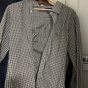 Ralph Lauren skjorta - Säljer en klassisk brun och vit rutig skjorta från Ralph Lauren med broderad logga på bröstet. Skjortan har lång ärm och är tillverkad i bomull. Perfekt för en stilren och tidlös look.