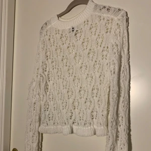 Vit stickad tröja - Säljer en vit stickad tröja med fint hålmönster och ribbade muddar. Tröjan har lång ärm och rund halsringning, perfekt för lager-på-lager och en mysig stil.
