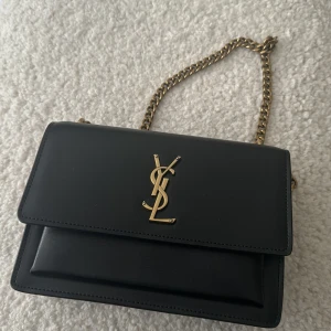 Svart handväska  - Säljer en svart handväska  med lock och kedjerem. Oanvänd. 