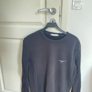 Svart sweatshirt från Off-White med färgglad logga - Svart sweatshirt från Off-White med liten vit text framtill och stor, färgglad logga i blått, rosa och gult på ryggen. Tröjan har rund halsringning och långa ärmar. Perfekt för dig som gillar streetwear och vill sticka ut.