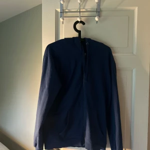 Mörkblå hoodie med dragkedja - Säljer en enkel och stilren mörkblå hoodie med dragkedja och huva. Tröjan har långa ärmar och två fickor framtill. Perfekt för en avslappnad look.