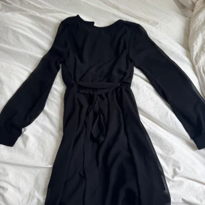 Svart långärmad klänning med knytband från NA-KD - Svart långärmad klänning från NA-KD i storlek 32. Endast använd en gång. Går till ovanför knäna på mig som är ca 170 cm. 