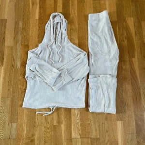 Beige ribbade mjukisbyxor med matchande hoodie - Säljer ett set med beige ribbade mjukisbyxor och matchande hoodie med huva och dragsko. Byxorna har en relaxed passform och är perfekta för en avslappnad stil. Materialet är mjukt och stretchigt för extra komfort. 