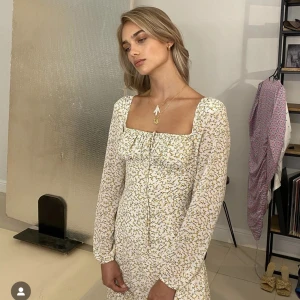 Blommig långklänning från Adoore - Superfin långklänning från Adoore i ljus färg med små gula blommor. Klänningen har lång ärm, markerad midja och fyrkantig ringning. Perfekt för vår och sommar, med dragkedja i sidan och mjukt, lätt material.