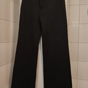 Svarta kostymbyxor Filippa K - Snygga svarta kostymbyxor från Filippa K i storlek XS. Byxorna har en snygg klassisk rak passform med dragkedja och knapp.        Mått: 102 cm lång, 76 cm innerbens längd, 35,5 cm waist.                                                   De är använda nån enstaka gång, så är i praktiken som nya. Kvalitetsmaterial i viskos, polyamid och elastan gör byxan lätt elastisk och fin form.
