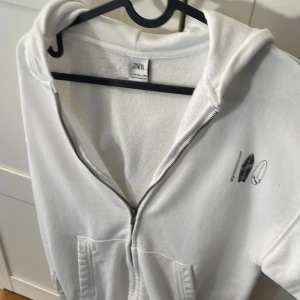 Vit hoodie med dragkedja från Zara - Vit hoodie från Zara med dragkedja framtill och fickor. Perfekt för sköna sommardagar. Storlek 13-14 cm 164