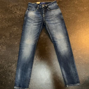 Blå jeansbyxor från Scotch & Soda - Snygga blå jeansbyxor från Scotch & Soda med lätt slitna detaljer framtill. Jeansen har regular slimfit passform och raka ben, perfekt för en avslappnad stil. Mörkblå tvätt med ljusare partier på lår och knän. Stl 30/32