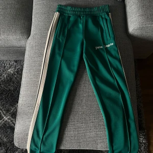 Gröna Palm Angels mjukisbyxor - Säljer ett par autentiska gröna mjukisbyxor från Palm Angels med vita sidoränder och elastisk midja. Byxorna har ett antal små brännmärken se bild 4-5. Utöver de är dem i nyskick.