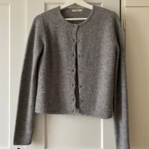 Grå stickad kofta från Gina Tricot - Mysig grå stickad kofta från Gina Tricot med rund halsringning och knappar framtill. Koftan har lång ärm och en rak, något croppad passform. Perfekt att styla över en topp eller klänning. Endast använd en gång, så näst in till helt ny💕