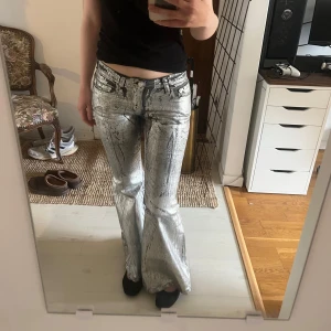 Silvriga bootcut-byxor  - Säljer ett par unika silvriga bootcut-byxor med glittrig finish och abstrakt mönster. Perfekta för dig som vill sticka ut med en cool och trendig look. Jag är 165 och jag har tidigare lagt upp byxorna då de var för långa ursprungligen💕