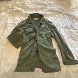 Grön overshirt med knappar - Säljer en grön overshirt med knappar framtill och två bröstfickor. Jackan har lång ärm och klassisk krage, perfekt att slänga över en t-shirt. Enkel och stilren modell som passar till mycket.
