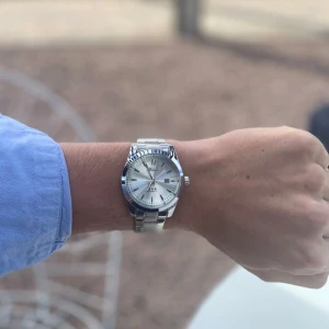 Silverfärgad herrklocka med metallarmband från Doventi  - Stilren silverfärgad klocka från Doventi med klassiskt rund urtavla och metallarmband. Urtavlan är vit med tydliga index och datumvisning. Perfekt accessoar för dig som gillar tidlös design och kvalitet.