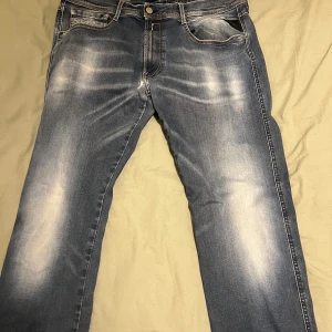 Replay Hyperflex jeans i blå denim - Säljer ett par Replay Hyperflex jeans i klassisk blå tvätt med snygga slitningar och kontrastsömmar. Jeansen har fem fickor och normal passform. Perfekta för dig som gillar bekväma och stilrena jeans med lite stretch. Tyvärr så är det bristningar i grenen som man nästan inte ser när man har på sig dem. Och taggen har lossat på ena under sidan 