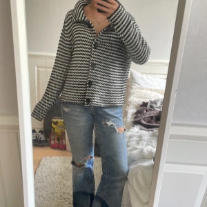 Svartvit rutig cardigan jacka - Säljer en svartvit cardigan jacka med rutigt mönster och stora svarta knappar. Jackan har lång ärm, krage och en avslappnad passform. 