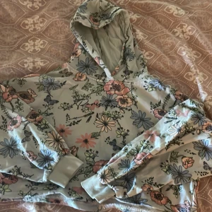 Magtröja Blommig hoodie från Ellos - Superfin hoodie från Ellos med blommigt mönster i pastellfärger. Tröjan har huva, långa ärmar och ribbade muddar. Perfekt för dig som gillar en avslappnad och söt stil.