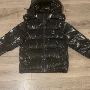 Svart pufferjacka från Trapstar - Säljer en glansig svart pufferjacka från trapstar med av och på tagbar huva. Jackan är använd några gånger men är i ett mycket fint skick där bland annat plasten på knapparna sitter kvar. Kom privat för flera bilder, priset kan diskuteras 