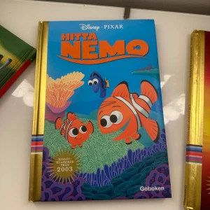 Hitta Nemo - Säljer boken 'Hitta Nemo' från Disney Pixar. Omslaget är blått med färgglada illustrationer av Nemo, Marlin och Doris under havet. Boken har guldfärgad rygg och är utgiven av Goboken. Perfekt för dig som gillar äventyr och hav.