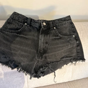 Svarta jeansshorts med fransar från Zara - Snygga svarta jeansshorts från Zara med fransig kant nertill. Klassisk femficksmodell och knäppjylf.