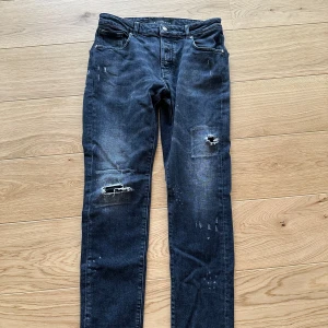 Svarta slitna jeans från Richmond - Säljer ett par svarta jeans från Richmond med slitningar och hål på benen. Jeansen har klassisk femficksdesign, knapp och dragkedja i gylfen samt raka ben. Perfekta för en avslappnad och trendig look.