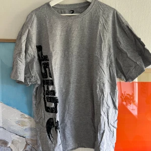 Grå t-shirt från GASP - Säljer en grå t-shirt från GASP i storlek XXL. T-shirten har ett stort svart tryck med GASP-loggan både fram och bak. Klassisk rund hals och korta ärmar. Perfekt för dig som gillar sportig och avslappnad stil.
