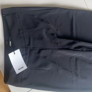 Svarta kostymbyxor från Bik Bok - Snygga svarta kostymbyxor från Bik Bok med klassisk passform och diskret dragkedja i sidan. Byxorna har hög midja och raka ben, perfekta till många olika looks. Stilrena och enkla att matcha med olika toppar.