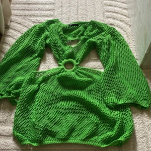 Grön stickad klänning med cut-out och ringdetalj - Säljer en knallgrön stickad klänning med lång ärm och cool cut-out framtill. Klänningen har en ringdetalj i midjan och är gjord i ett nätliknande material. Perfekt för stranden