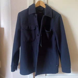 Mörkblå overshirt från Matinique - Säljer en stilren mörkblå overshirt från Matinique. Jackan har två stora bröstfickor med knappar och klassisk krage. Perfekt lager-på-lager-plagg med knappstängning framtill. Helt oanvänd (1499kr nypris)