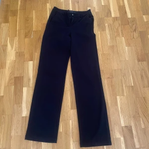 Svarta kostymbyxor från Vero Moda - Klassiska svarta kostymbyxor från Vero Moda med raka, vida ben och hög midja. Perfekta för en stilren look och enkla att matcha med olika toppar. Byxorna har diskret stängning framtill och är tillverkade i ett mjukt material.