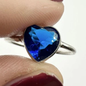 Hjärtslipad blå topasring i silver – äkta ädelsten med djup glans - Elegant silverpläterad ring med äkta hjärtslipad blå topas – ingen labbsten! Den djupblå nyansen gnistrar vackert och gör ringen till ett perfekt smycke för både vardag och fest. Topas sägs stärka intuition, kärlek och självförtroende. Ny/oanvänd och i mycket fint skick. Storlek ca 18,25 (innerdiameter ca 18,5 mm).  Ingen prutning, men bundlerabatt erbjuds! 
