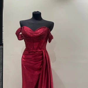 Röd axelbandslös balklänning med paljetter o sammet tyg  - Säljer en elegant vinröd långklänning med axelbandslös design och draperad överdel dekorerad med paljetter. Klänningen har markerad midja, figurnära passform och vacker drapering längs kjolen. Perfekt för bal eller fest! Tyget är sammet liknande och gör att klänningen faller elegant! 