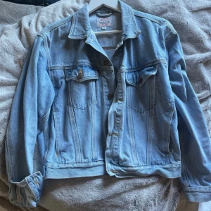 Ljusblå jeansjacka - Klassisk ljusblå jeansjacka med knappar framtill och två bröstfickor med lock. Jackan har en rak passform och långa ärmar. Perfekt nu för sommaren 