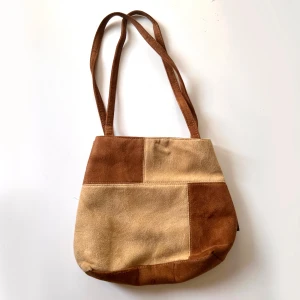 Brun och beige axelväska i mocka - Säljer en snygg 2000s axelväska i fejkmocka med patchwork-design i brunt och beige. Väskan har två långa axelremmar och två fack som stängd med dragkedja. använt skick. Klicka på köp nu <3