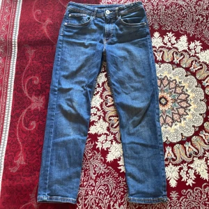 Blå jeansbyxor i relaxed fit - Säljer ett par blå jeansbyxor i relaxed fit. De är tillverkade av denim och har en tapered leg design. Byxorna är i storlek 152 och är tillverkade i Pakistan. Perfekta för en avslappnad och bekväm stil!