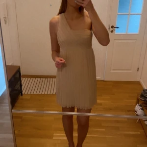 One-shoulder klänning  - Plisserad one shoulder kort klänning som faller väldigt fint. Har en ljus, puderrosa färg. Använd 3 gånger och ser som ny ut på utsidan. Underklänningens söm har "öppnat sig" lite (se sista bilden) de nedre 20 centimetrarna, inget som syns/stör.