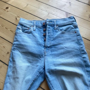 Ljusblå jeans från Mother - Säljer ett par snygga ljusblå jeans från Mother. De är högmidjade och har en knappgylf med flera knappar framtill. Baktill finns två fickor med en cool broderad detalj. Perfekta för en avslappnad och stilren look!