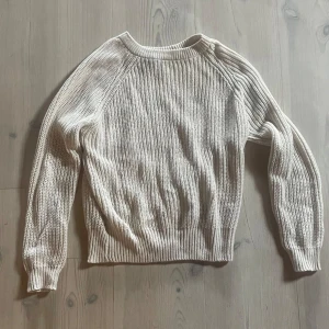 Vit stickad tröja från Label Collection - En vit stickad tröja från Lager 157. Tröjan har långa ärmar och en ribbad struktur. Den är varm och bekväm, perfekt för kyligare väder.