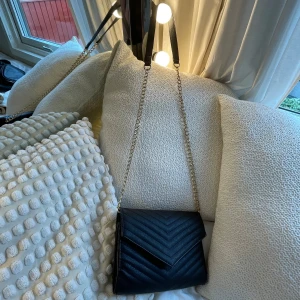 Svart axelväska med kedja - Denna fina väskan är köpt nyskick secondhand. Av mig är den använd ca 3 gånger. Kedjan har inga missfärgningar. Den har 2 större fack och 2 små. Prisförslag är uppskattat! 💕Skriv för fler bilder och frågor!