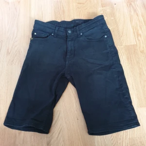 Svarta shorts från Forever - Säljer ett par svarta jeansshorts från tiger of sweden i storlek 28. De är gjorda av 92% bomull, 6% polybutylene terephthalate och 2% elastan, vilket gör dem både bekväma och stretchiga. Shortsen har en dragkedja och knapp framtill, samt fem fickor - två fram, två bak och en liten myntficka. Perfekta för sommarens alla äventyr!