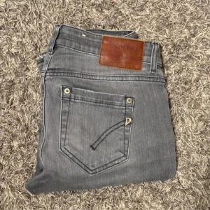 Grå jeans från Dondup - Säljer ett par snygga grå jeans från Dondup i storlek 29. De är i bra skick och har en klassisk femficksdesign med en dragkedja och knapp framtill. Jeansen har slimmade passform, ass feta