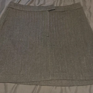 Grå kjol från Gina Tricot - Säljer en snygg grå kjol från Gina Tricot i storlek XL. Kjolen  är gjord av ett bekvämt material. Den har en dragkedja framtill och en knapp för extra säkerhet. Katt finns i hemmet! Alla kläder jag säljer är rollade och nytvättade ✨