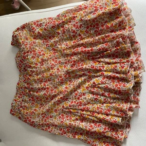 Blommig kjol från Amisu - Säljer en superfin blommig kjol från Amisu i storlek S/36. Kjolen har ett färgglatt blommönster i rött, gult och grönt på en vit bakgrund. Den är perfekt för sommaren och har en luftig och bekväm passform. Passar både till vardags och fest! 🌸