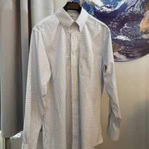 Vit och blå rutig skjorta från Brooks Brothers - Säljer en klassisk vit och blå rutig skjorta från Brooks Brothers. Skjortan är i nyskick och har långa ärmar med knappar. Den är tillverkad av 100% bomull och är perfekt för både vardag och fest. Passformen är normal och materialet är mjukt och bekvämt. Perfekt för att se stilren ut!