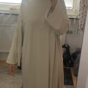 Beige långklänning med vida ärmar - Säljer en superfin beige abaya med vida ärmar. Klänningen är i ett ribbat material som ger en snygg textur och är perfekt för vardag. Den har en lös passform som gör den bekväm att bära hela dagen. Den är helt ny aldrig använd pga för kort för mig som ni kan se i sista bilden. Jag är 175 cm. Perfekt för varmare väder, luftig. 